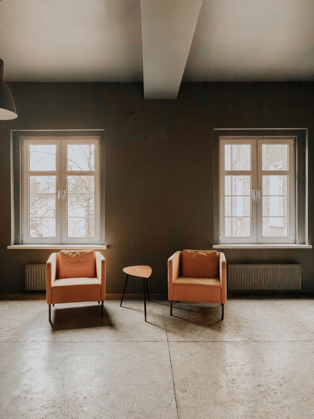 Two upholstered chairs turned towards a small table between two daylit windows