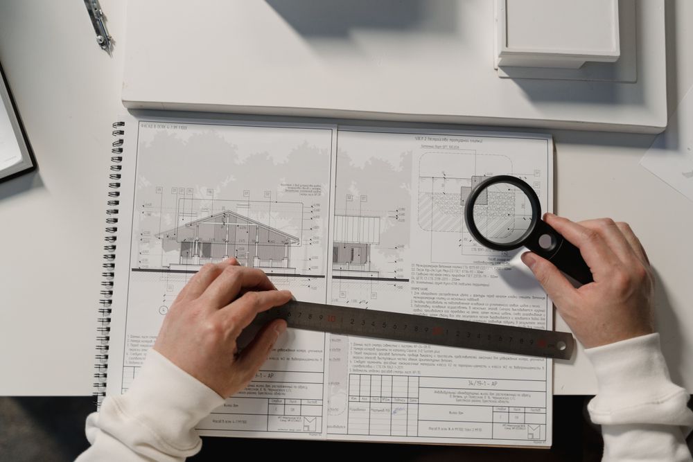 Hands laying a rule and a glass across a drawn plan on a working desk